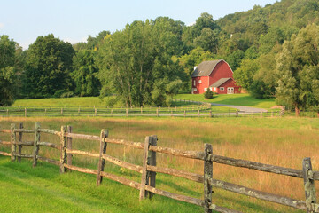 Naklejka premium Rural summer landscape near Kent in Connecticut with a rail fence in the front and a red barn in the distance