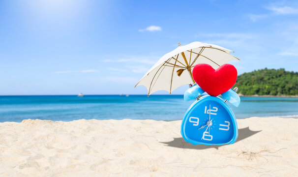 Blue alarm clock under umbrella over tropical beach background, summer outdoor day light, it's summer time