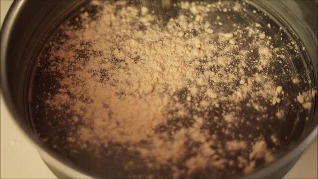 Close-up of fine powder being sifted into a shiny metal pot