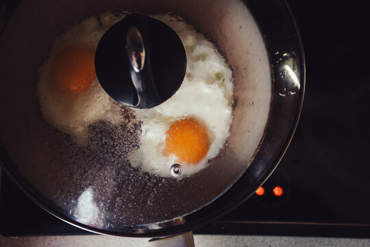Two fried eggs in a pan under a glass lid