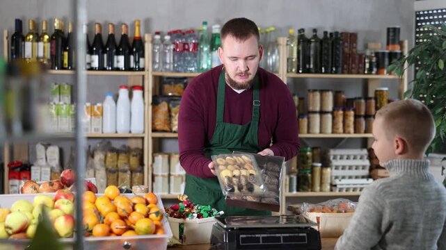 Friendly salesman kindly assisting little boy purchasing cookies in grocery store 