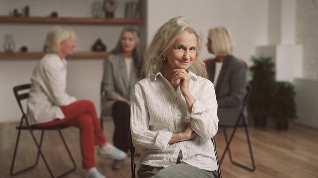 Self-confident aged lady smiling to camera, portrait in room for group therapy. Happy and empowered woman of 60 years old looking at camera, stay healthy and active in old age, women support group