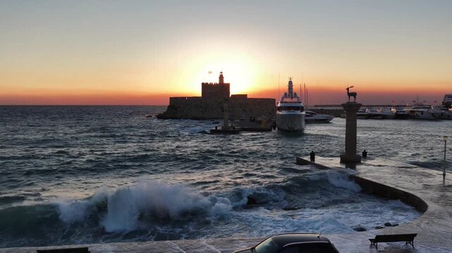 Sunset waves crash on Rodos shore by historic fort and deer statue