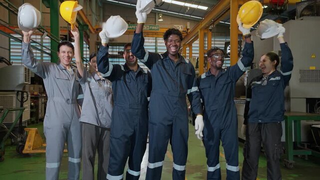 United Workforce: A unified team of industrial workers raise their helmets in a symbol of teamwork and shared goals, celebrating their accomplishments within their workshop. 