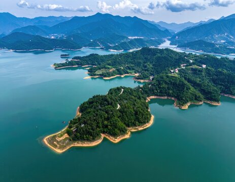 An aerial view showcases a lush, green island nestled within a winding, turquoise reservoir surrounded by rolling mountains.