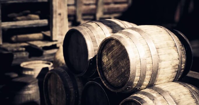 Several rustic, wooden barrels are stacked in an outdoor storage area. The sunlight casts warm tones on the barrels, highlighting the grain of the wood and the settings rustic charm.