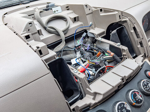 Exposed car dashboard with tangled wiring and removed stereo unit, closeup of beige interior, scattered connectors and cables, DIY installation scene