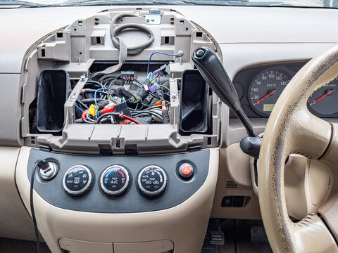 Partially disassembled dashboard with exposed wiring and climate controls, aftermarket stereo installation mood with technician workflow implied, beige steering