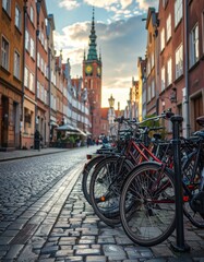 Obraz premium A charming cobblestone street in a historic European city showcases a row of parked bicycles leading towards a picturesque clock tower bathed in the warm glow of the setting sun.