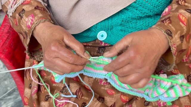 Old lady knitting colorful sweater. Elderly female hand knitting from wool. Knitting sweater with wrinkly hands. close-up hands knitting sweater. Colorful Crochet with wrinkly hands. 