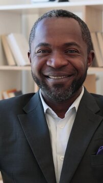 A professional African American man with a beard smiles warmly while wearing a suit and a purple pocket square, suggesting confidence and approachability