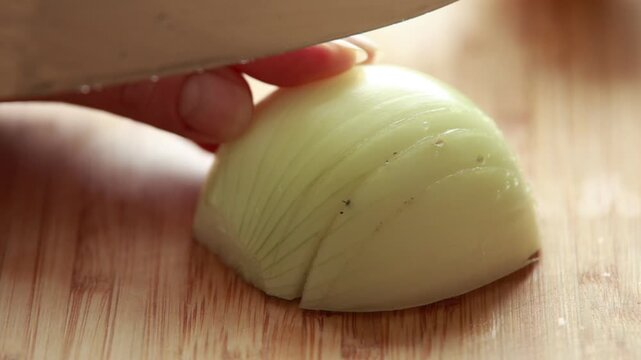 Close-up of woman's hands chopping a fresh onion on a rustic wooden cutting board, bright natural light