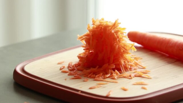 Close-up of grated fresh carrot on a rustic wooden cutting board in bright natural light