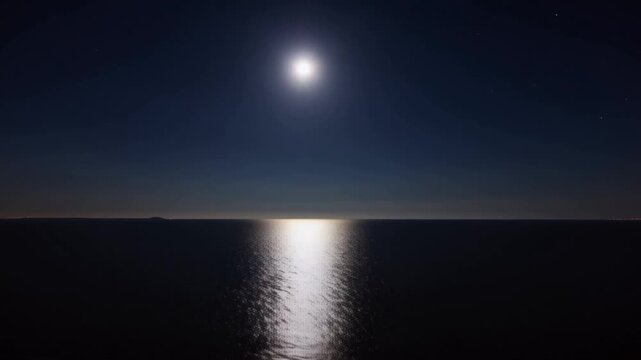 Static long exposure shot from a seaside at night, a moon creating a bright, shimmering silvery path on the perfectly smooth, dark surface of the water, concept of nocturnal serenity