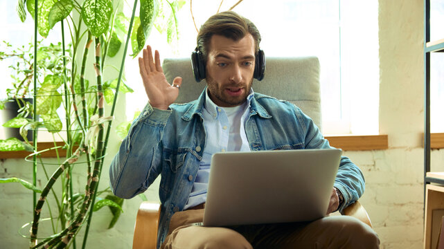 Man with headphones reacting surprised during online coaching call on laptop. Concept of client feedback, emotional response, remote consultation, and online coaching.