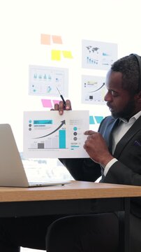 An African American man in a suit points to a financial graph during a virtual meeting, showcasing business growth and data analysis