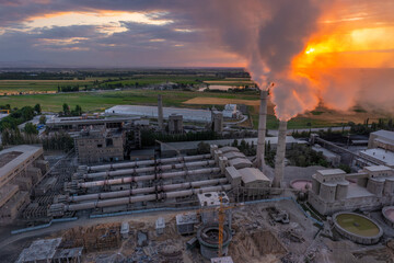 Aerial view of Industrial cement plant with smokestacks and agricultural fields at sunset