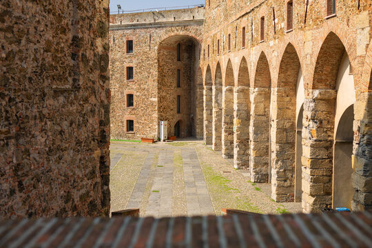 Interior view of the courtyard of the Medieval Fortress with Stone Arches of Priamar in Savona, Liguria, Italy. Close-up of an ancient fortified courtyard with a rustic stone arched gallery, medieval