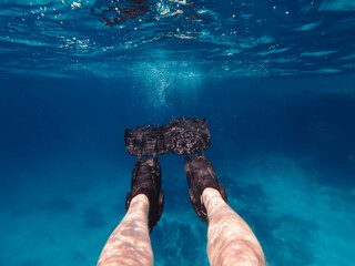 Point of view of a person wearing black flippers swimming underwater in the deep blue sea during a summer vacation © Dmitri