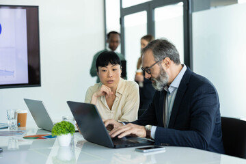 Obraz premium Diverse professionals working together in a modern office, planning strategies and discussing project data during a corporate meeting
