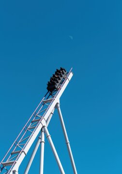 Black roller coaster train climbing steep steel track toward a clear blue sky, thrilling amusement park ride banner for travel and entertainment with copy space