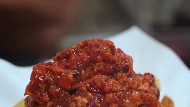 A vibrant, slow-motion close-up of a thick, textured red spicy chili sauce or savory chutney being poured or ladled onto a dish.