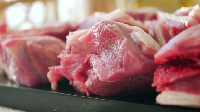 Raw meat cut into chunks on black tray fresh pork or beef close-up slow motion footage.