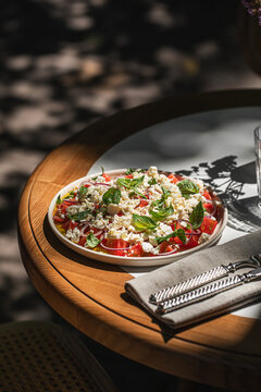 Fresh mediterranean salad with tomatoes cheese herbs and olive oil served on plate with sunlight and shadows