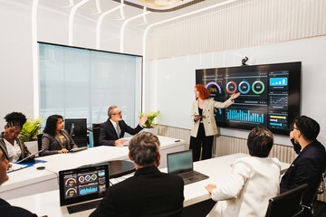 Professionals in a modern conference room review data dashboards on a large screen as a presenter...