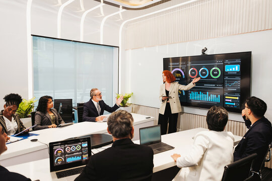 Professionals in a modern conference room review data dashboards on a large screen as a presenter leads a strategy meeting.