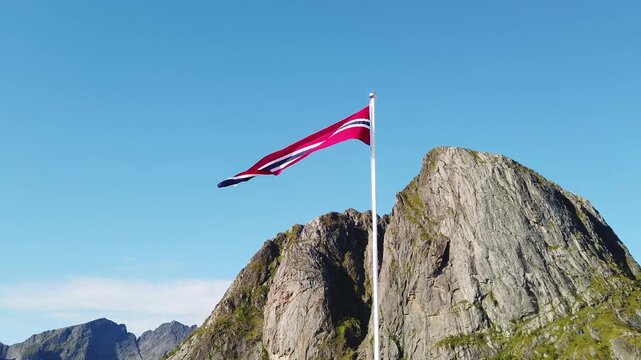 Norwegian flag waving over hamnoy mountain in lofoten islands