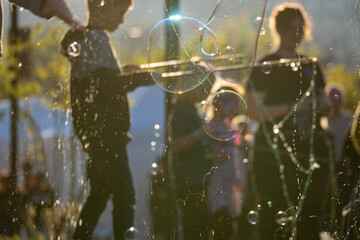 Soap bubbles and glittering spray drift through warm sunset light, with softly blurred people in the background, creating a dreamy festive atmosphere outdoors. © AS