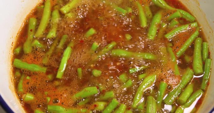Yardlong beans boiling in Thai sour curry (Gaeng Som), bubbling spicy-sour broth, showing cooking process