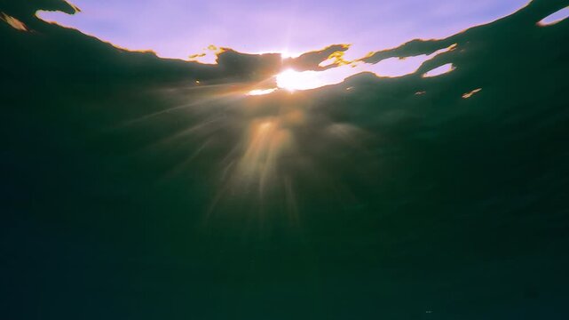 Bright sunlights penetrates through surface of water with ripples illuminating the sea depths, contre-jour, Slow motion of sun rays playing bright flashes below water surface with waves