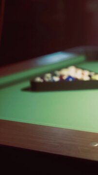 A group of friends gathers around a pool table in a local venue. They focus on the game as they strategize their next moves. Light from above shines on the green surface.