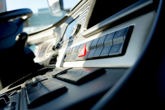 Modern truck dashboard with focus on the red hazard light button, captured in bright natural light, showcasing commercial vehicle interior details.