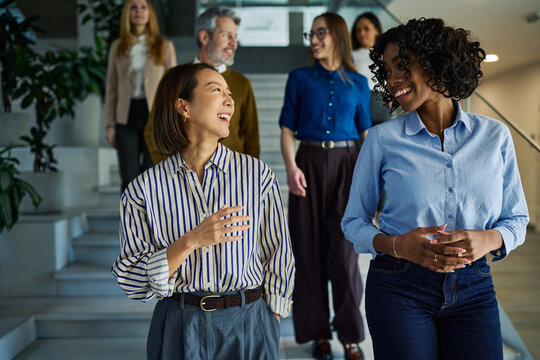 Diverse business colleagues walking on office stairs talking and smiling