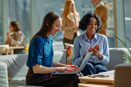 Diverse businesswomen collaborating using laptop in modern office lounge