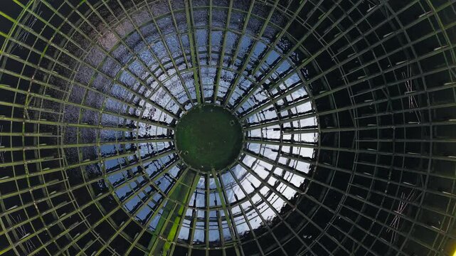 Circular steel lattice inside nuclear cooling tower with mirrored water surface and deep perspective. Power generation infrastructure concept connected to energy crisis and industrial technology