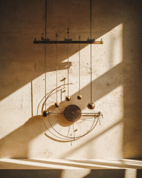 Sunlit geometric wall sculpture with brass spheres and orbital lines on textured plaster wall