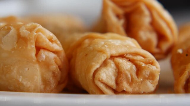 Close up motion of golden fried spring rolls on white plate, cinematic food footage.