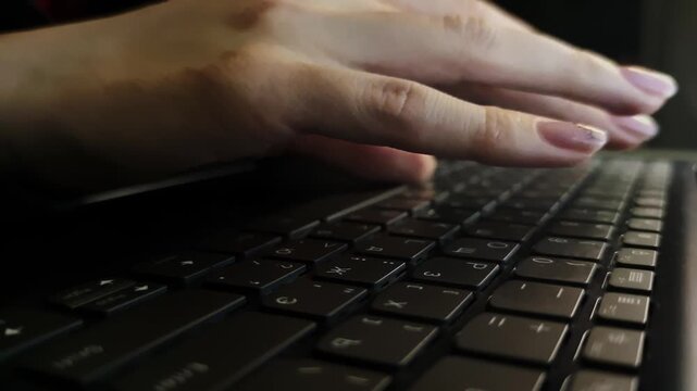Closeup view of female fingertips typing rapidly on laptop keyboard filmed in the evening. Caucasian woman is working distantly having deadline. She is creating electronic documents and spreadsheets 