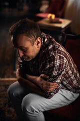 Obraz premium Man with headache, depression, sadness and loneliness sitting on a chair at home.