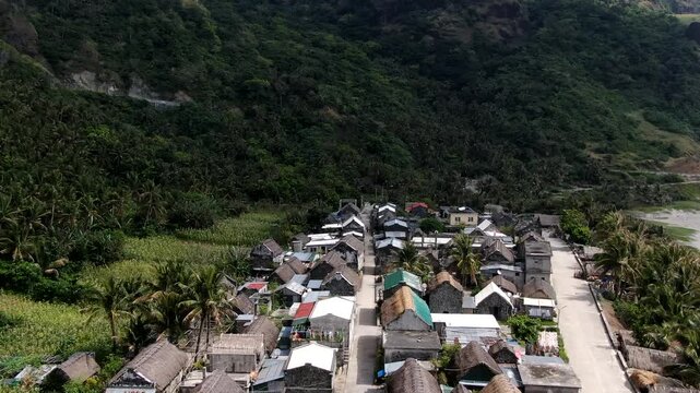 Aerial forward flight over the traditional Ivatan stone houses of Chavayan Village nestled under lush green mountains in Sabtang Island, Batanes, Philippines