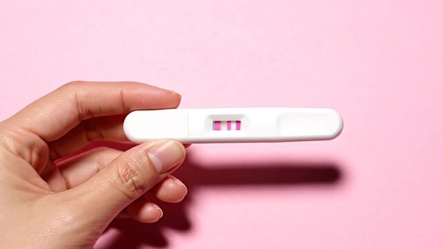 Positive pregnancy test held in a hand against a pastel pink background signifying anticipation and new beginnings