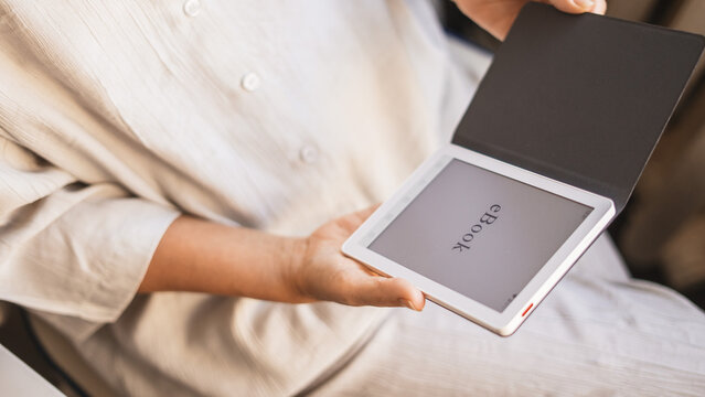 Woman holding ebook reader with cover in soft warm light at home. Concept digital reading, modern lifestyle, relaxation, comfortable learning, cozy atmosphere, mindfulness and peaceful leisure moment