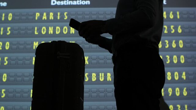 Traveler silhouette with luggage checks smartphone against a digital departures board listing paris and london, symbolizing international air travel, connection and planning
