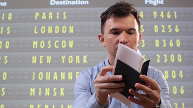 Man holding passport and boarding pass, studying the airport departure board to confirm flight details, gate and schedule before an international business or leisure trip, focused and intent