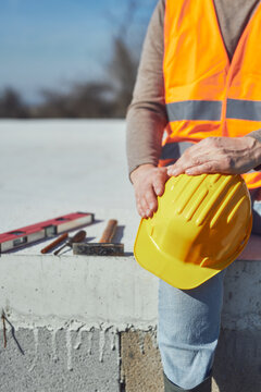 Construction worker working outdoors on a construction site, making a pause and holding a yellow hardhat.