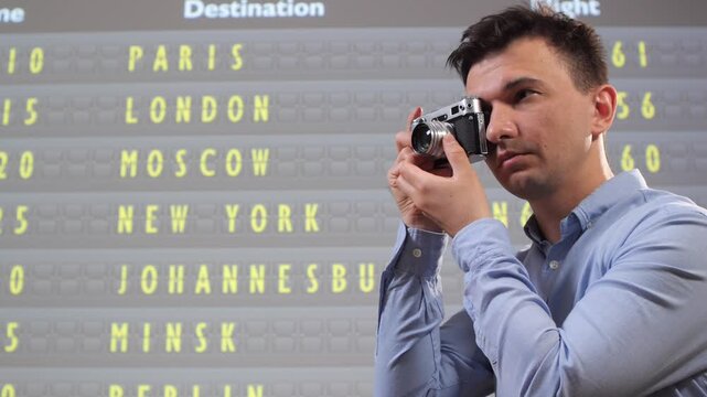 Man holding old film camera capturing information from a split flap display board showing various cities and flight numbers, symbolizing travel, hobby, and international connections